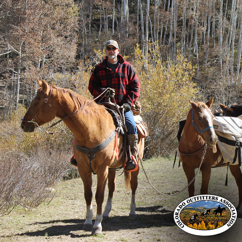 Bill Wilson on horseback leading a packhorse through autumn aspens